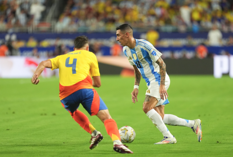Di Maria đi bóng trước sự áp sát từ Arias. Anh mang băng thủ quân và dẫn dắt Argentina sau khi Messi rời sân